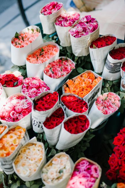A collection of fresh flower bouquets arranged in cylindrical paper wrapping, featuring a variety of roses in shades of pink, red, and peach. The bouquets are displayed on a dark surface, with some wr
