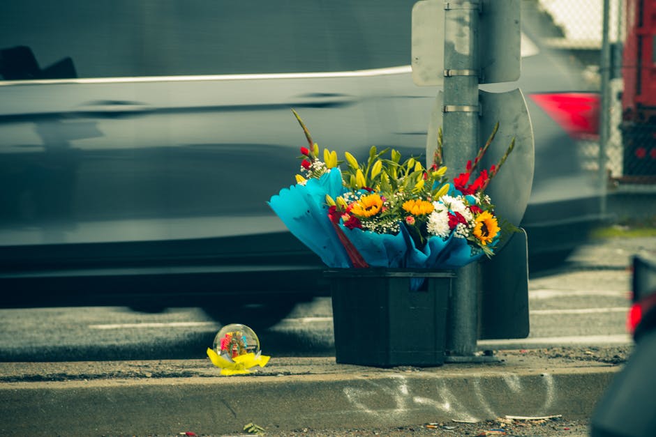 A vibrant bouquet of fresh flowers, including yellow sunflowers, red gladiolus, white chrysanthemums, and green foliage, arranged in a wrapped floral display with blue tissue paper and tied with a red