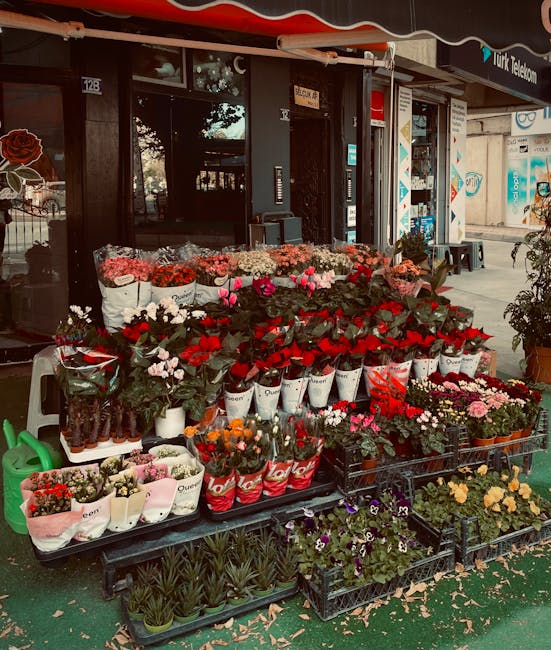 An outdoor flower stall in front of a shop, showcasing a variety of fresh floral arrangements including pink, red, white, and orange blooms. The display features wrapped bouquets in white, red, and pi